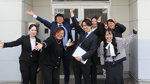 施設の前に集合し、笑顔でガッツポーズをするスタッフ一同